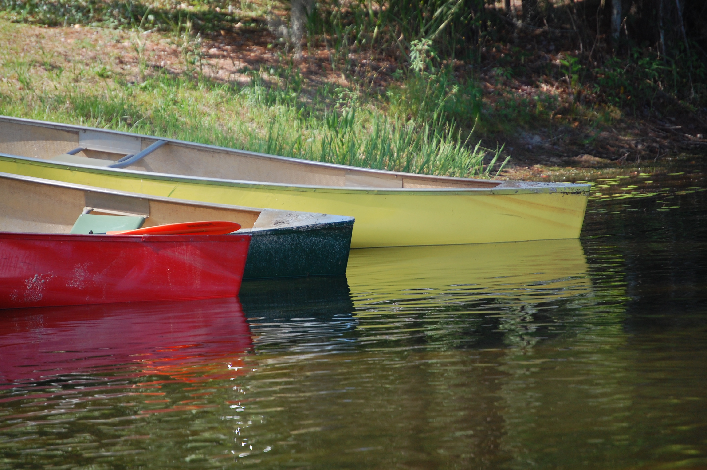 The edges of a red, black, and yellow canoe are dipping into lake water from the shore on the left side of the photo.