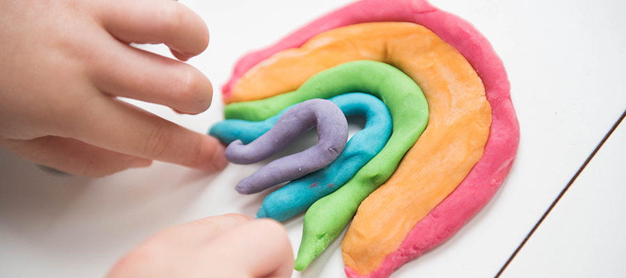 A child's fingers stretching playdough to make a rainbow