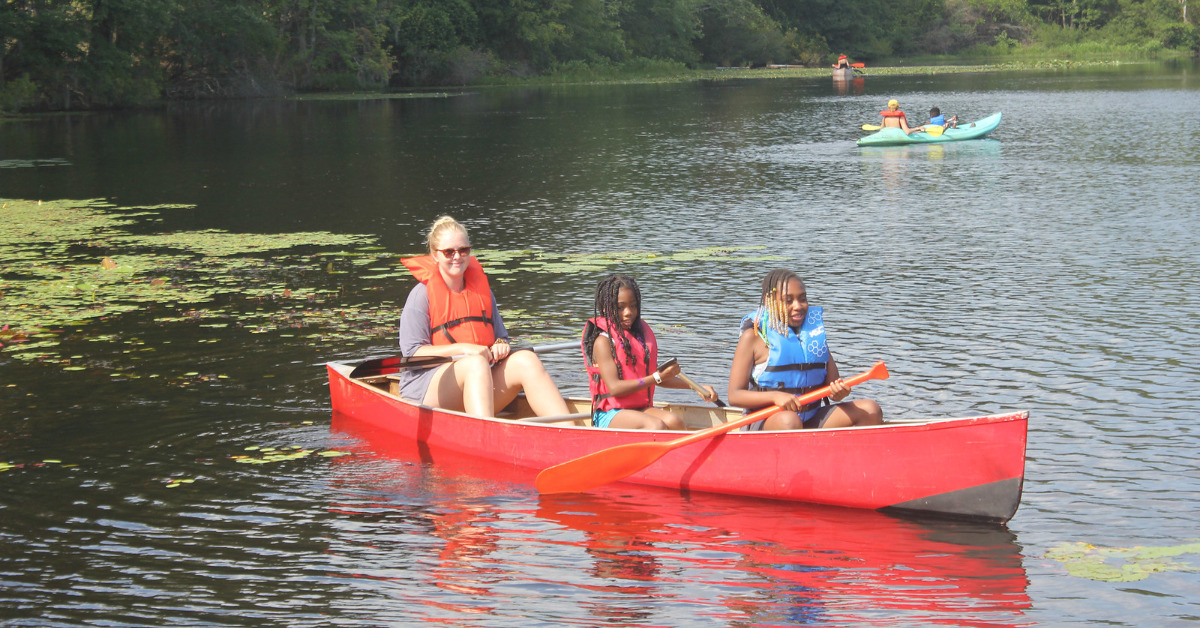 One female counselor and two campers are in a red canoe.
