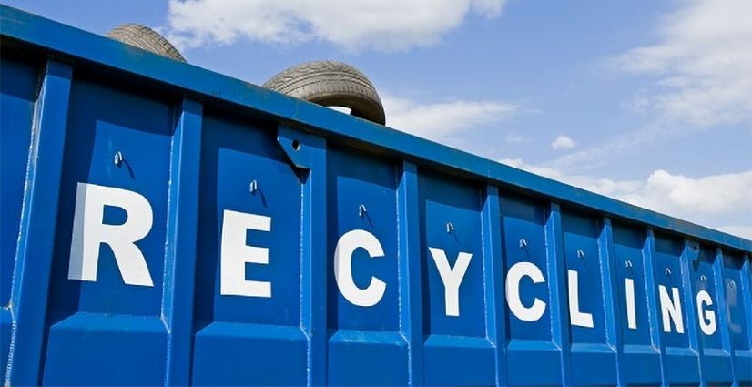 Blue, large dumpster with RECYCLING in white letters. Tire is resting on the top. Blue sky with clouds
